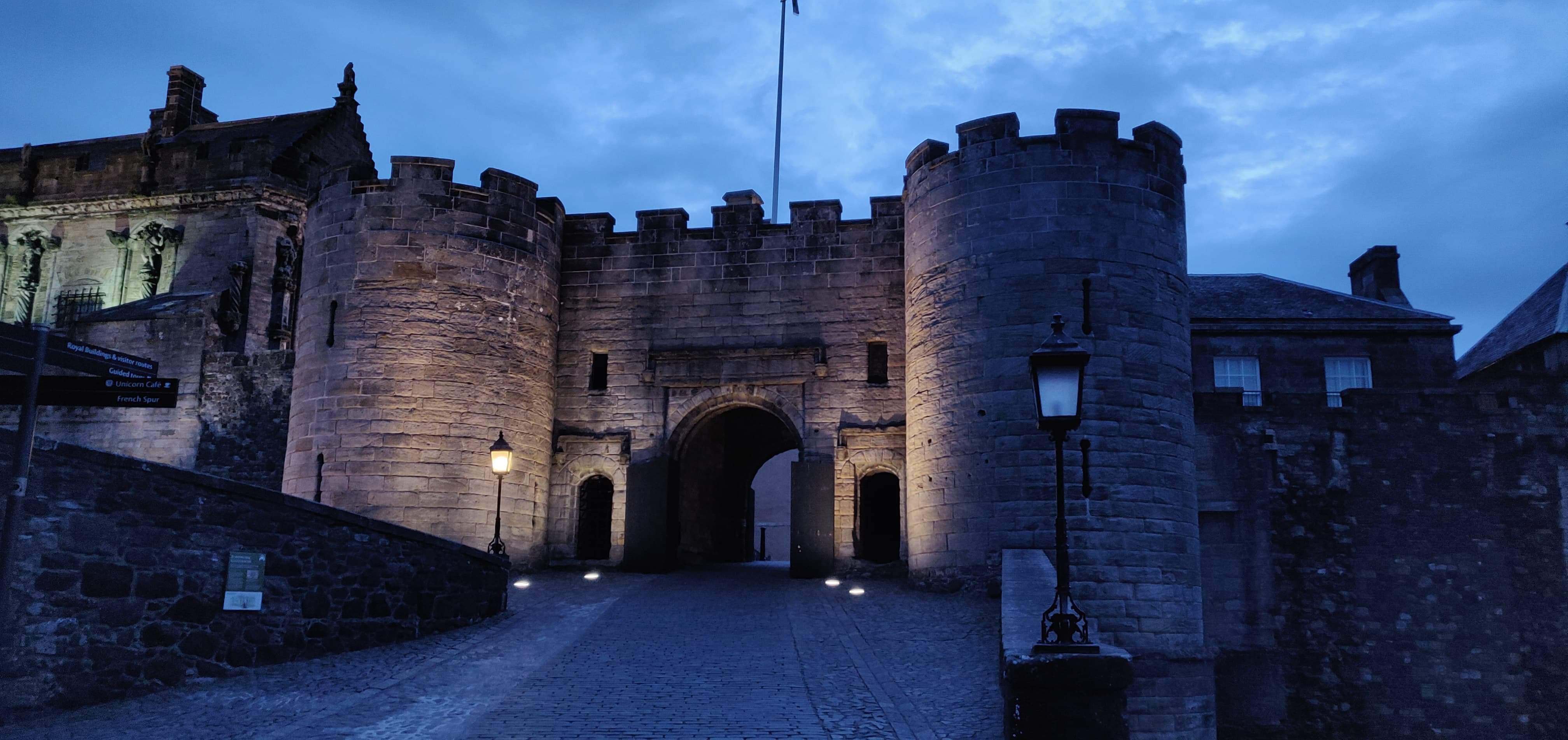 Two turret castle entrance lit up in the evening under a grey sky.