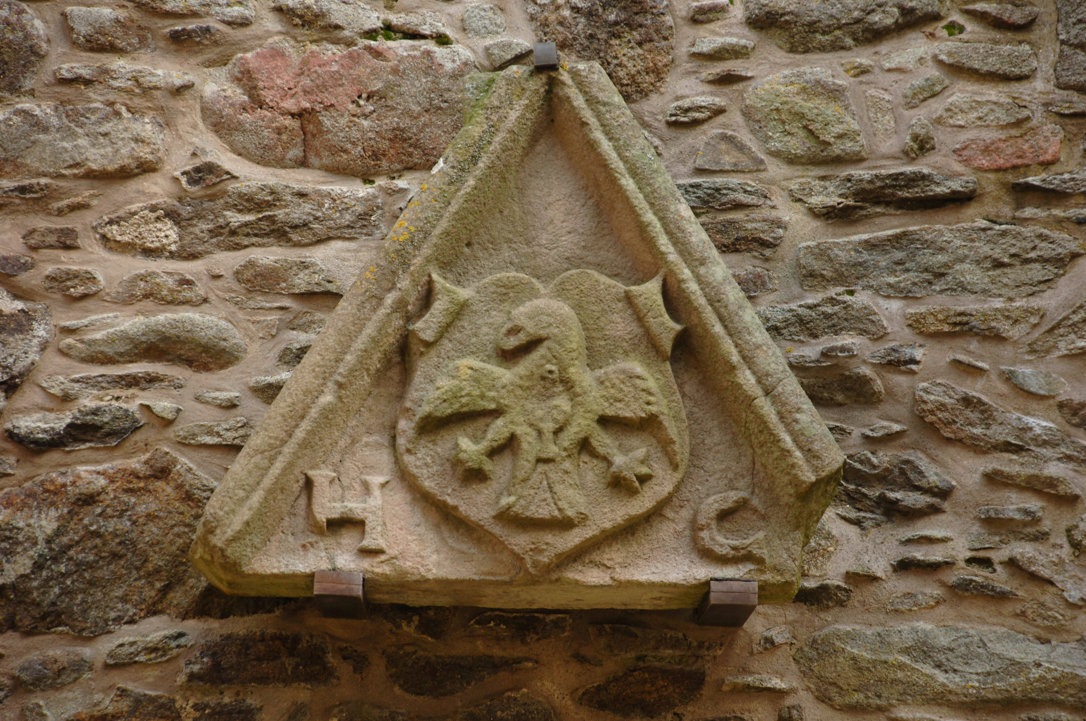 Carved stone heraldic panel set into a wall, featuring a winged creature, perhaps an eagle, and other decorative symbols.