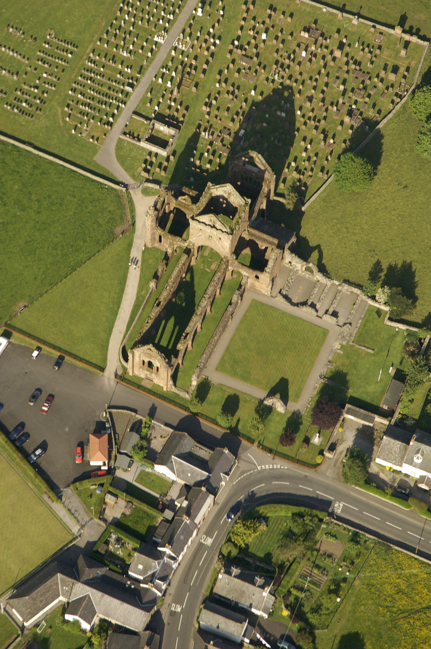 Aerial view of abbey ruin with graveyard, fields, carpark and road surrounding