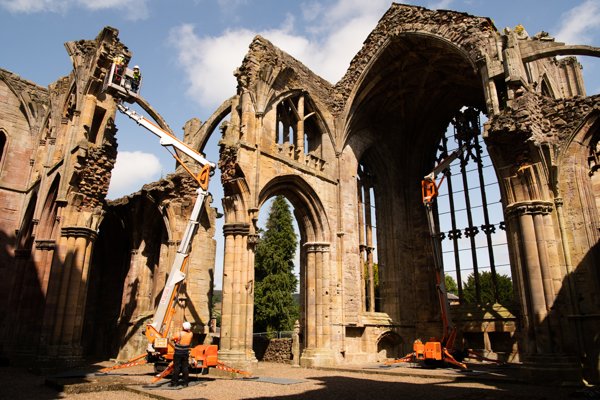 Engineers wearing personal protective equipment (PPE) while inspecting the masonry of an abbey from the top of two cherry pickers