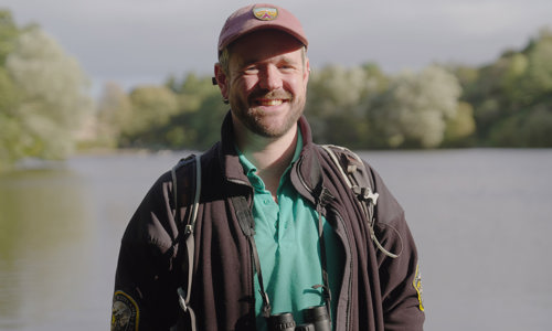 A Volunteer Ranger standing by a loch with trees around it