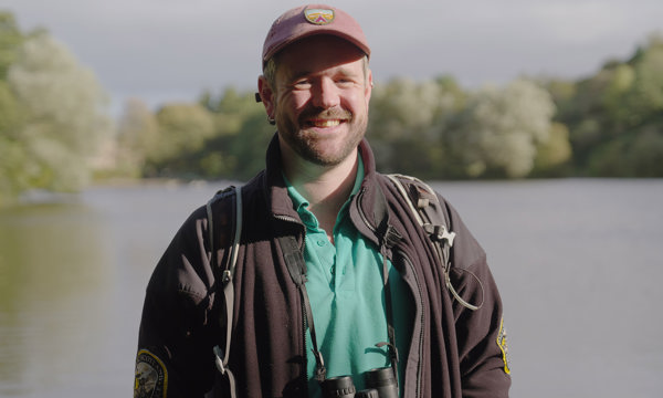 A Volunteer Ranger standing by a loch with trees around it