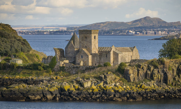 A beautiful abbey on an island surrounded by an estuary on a bright sunny day with hills in the background 