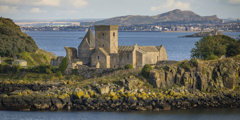 A beautiful abbey on an island surrounded by an estuary on a bright sunny day with hills in the background 
