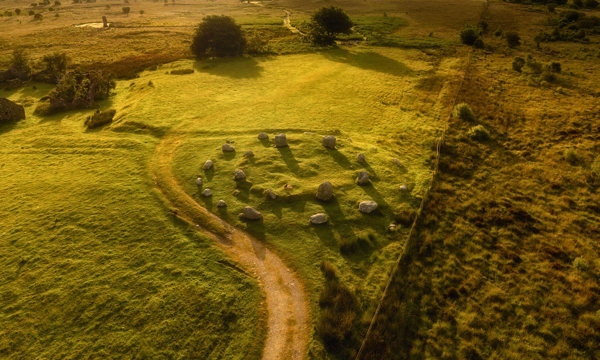 A standing stone circle is shown from above. There are fields on every side and the sunlight is golden