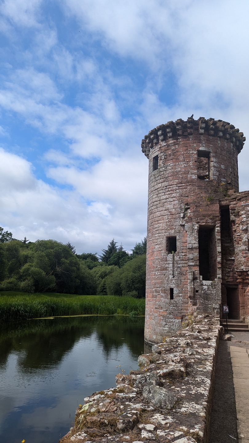 round stone tower next to a water filled moat with trees visible on the shoreline behind