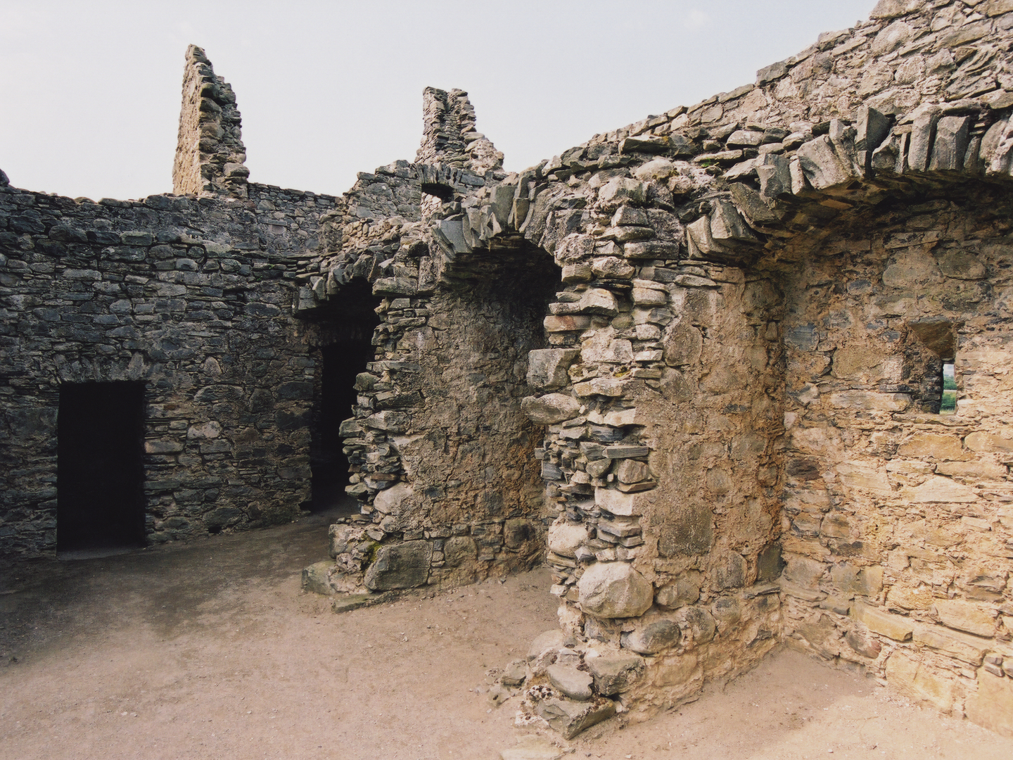 A historic stone wall, with three arches. You can see in one of the arches there is a small window inside of it. 
