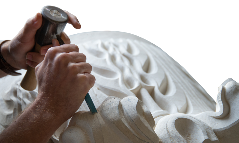 Hands holding tools and chiselling detail into a carved stone.