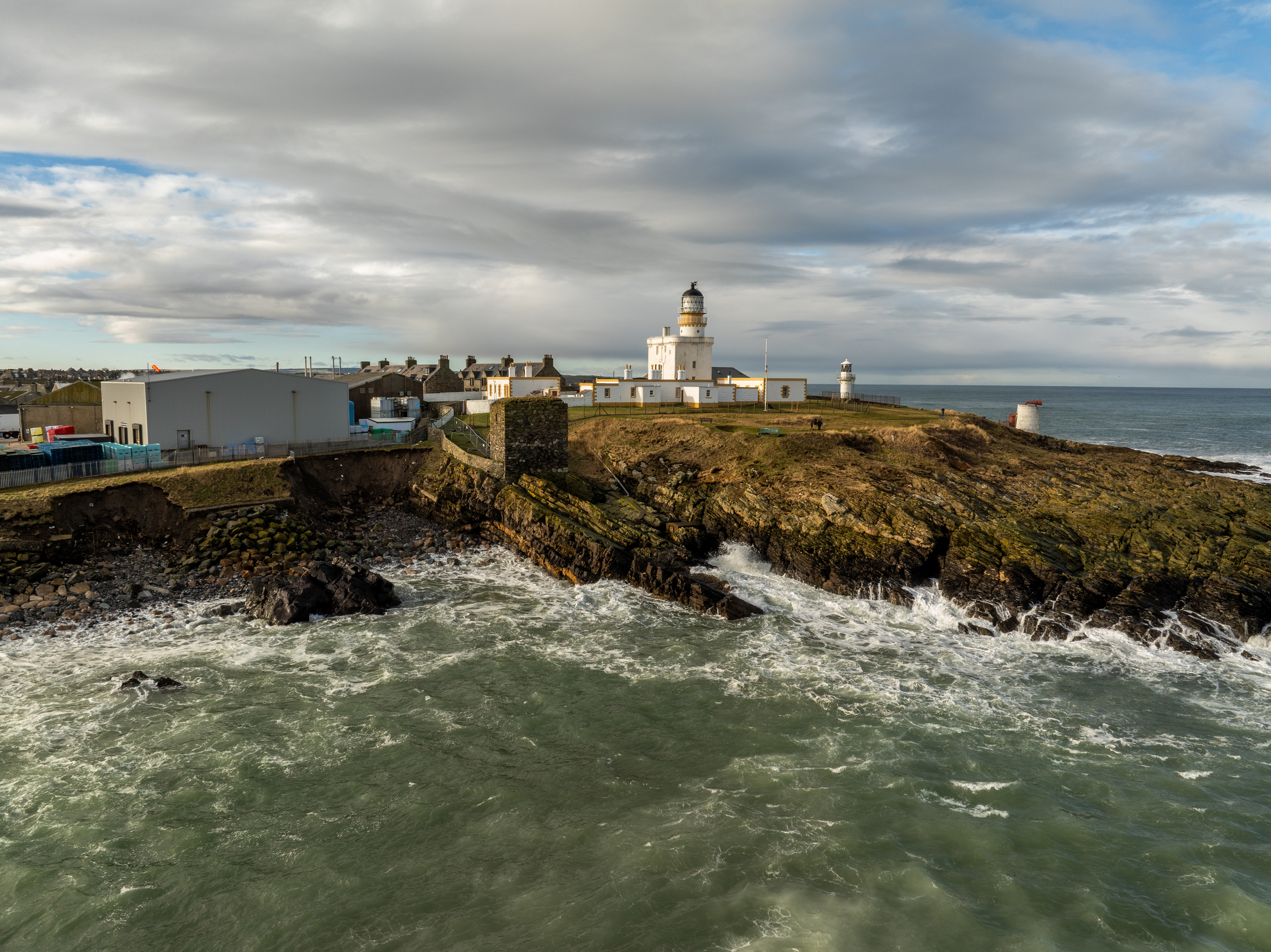 Aerial photo of a historic lighthouse on cliffs above a rough sea.