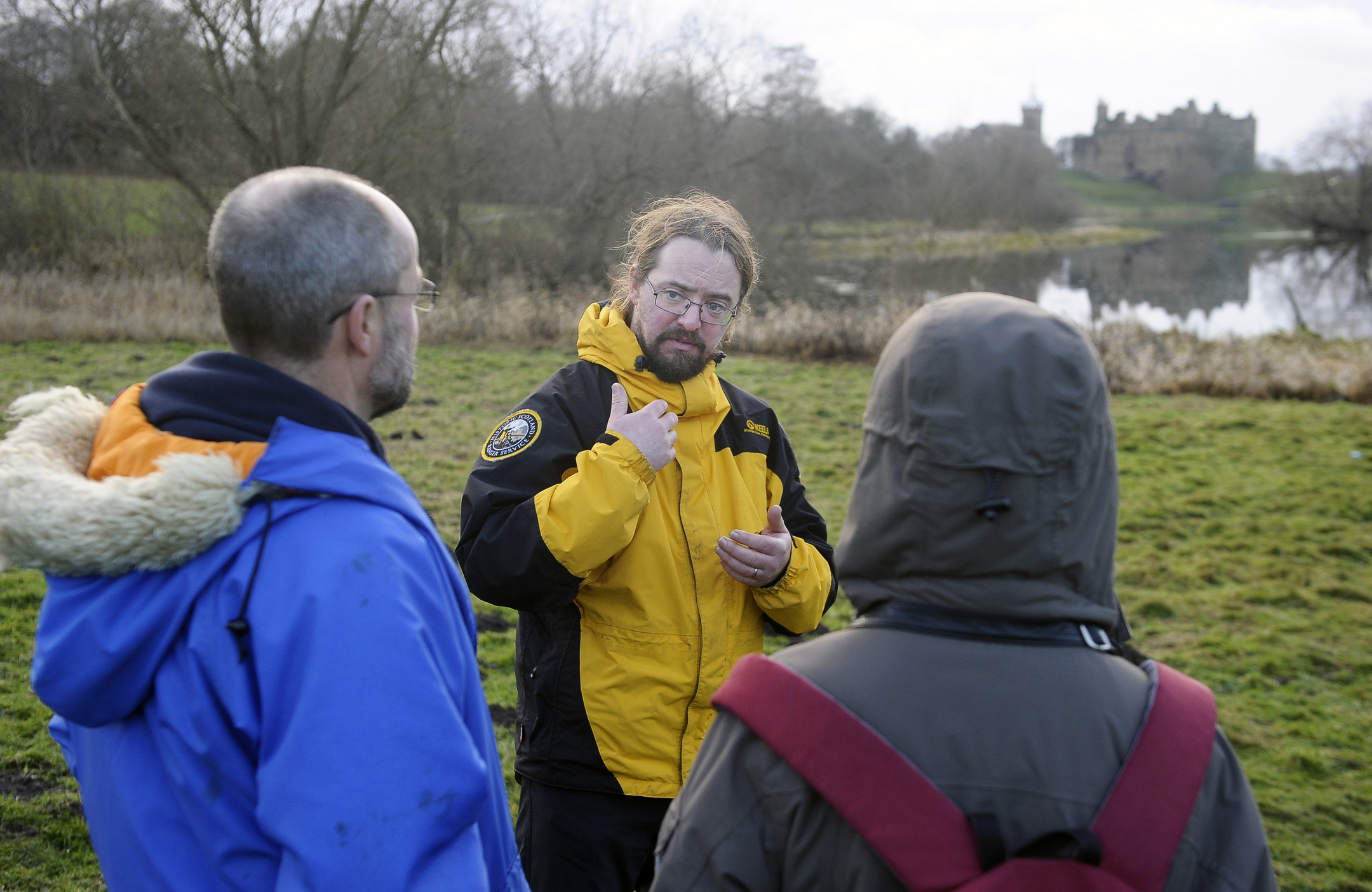 A ranger in a yellow jacket speaks to two visitors at Linlithgow Loch