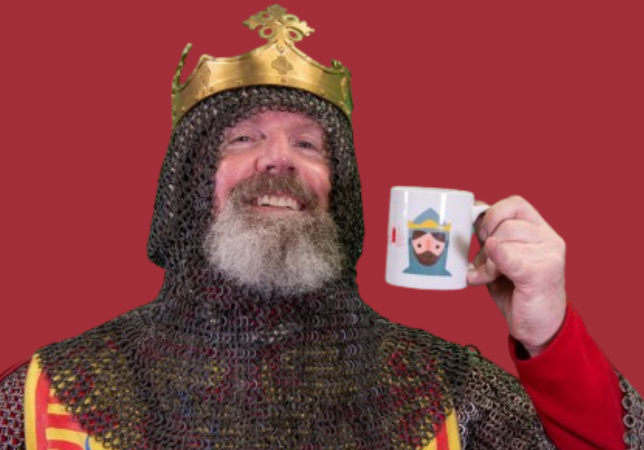 A man smiling wearing a crown and chainmail holding a Robert the Bruce mug