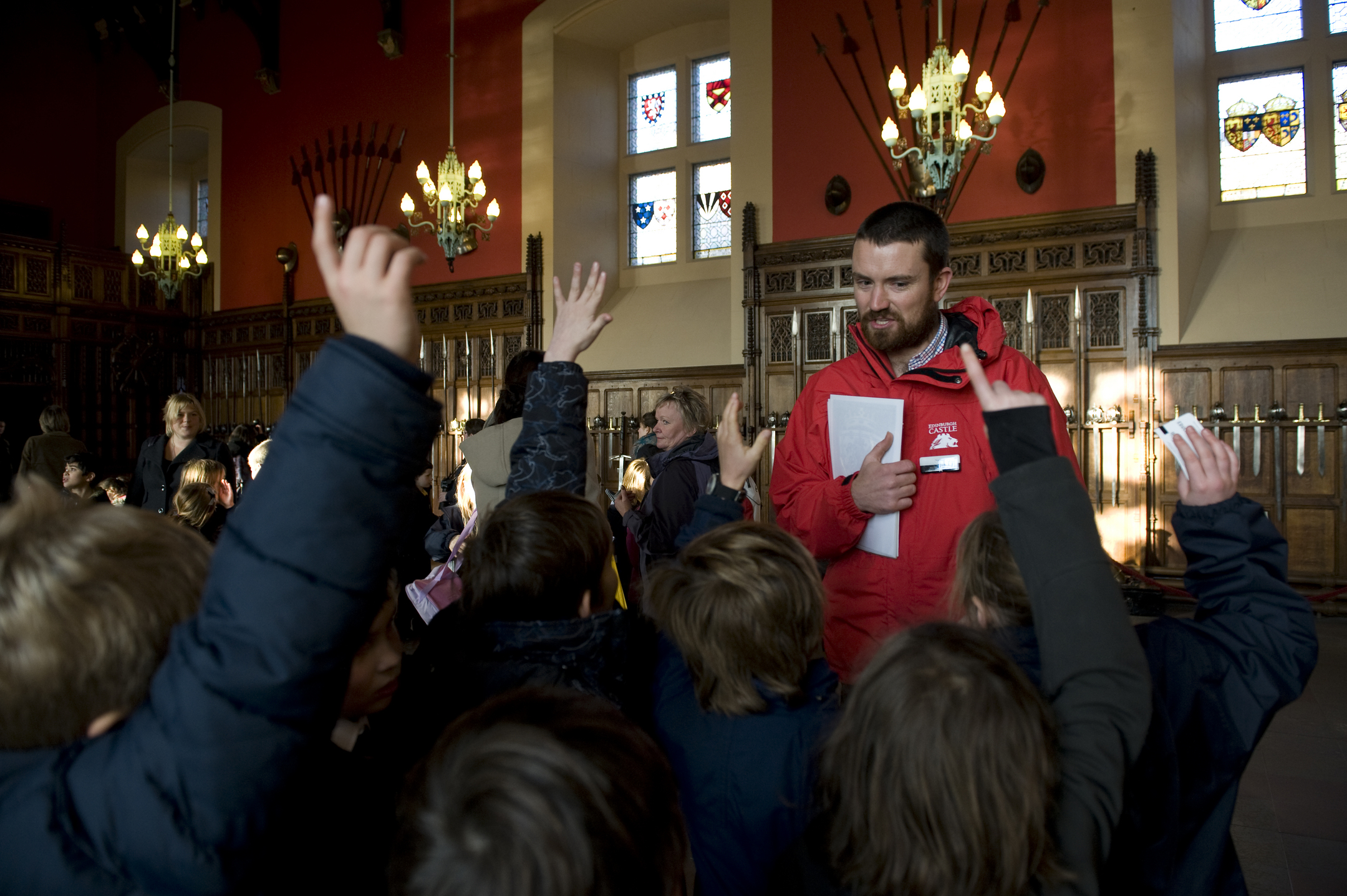 Pupils raise their hands to ask a question in a grand indoor room in a castle