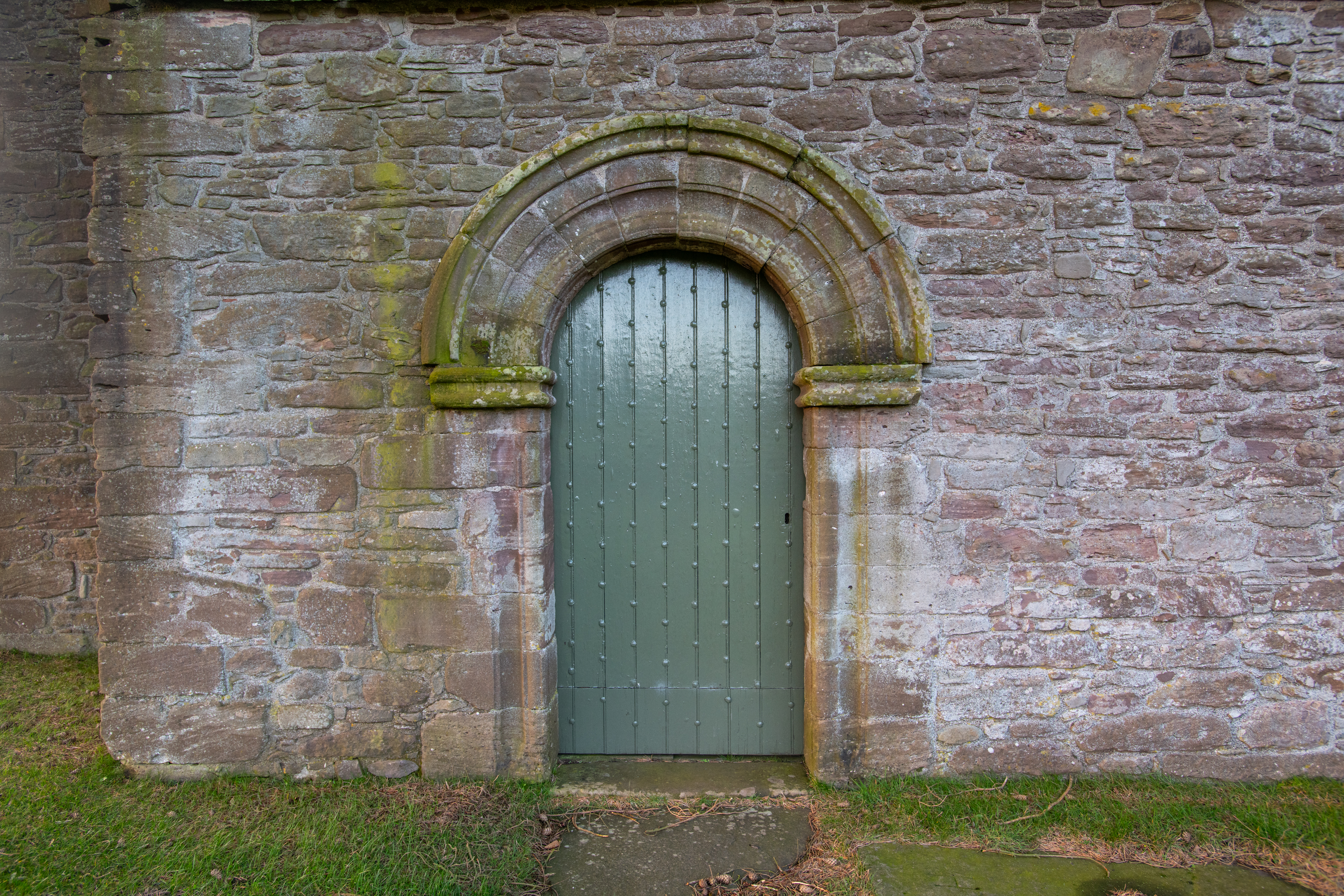 studded wooden door painted green, set in an arched doorway in a red stone wall