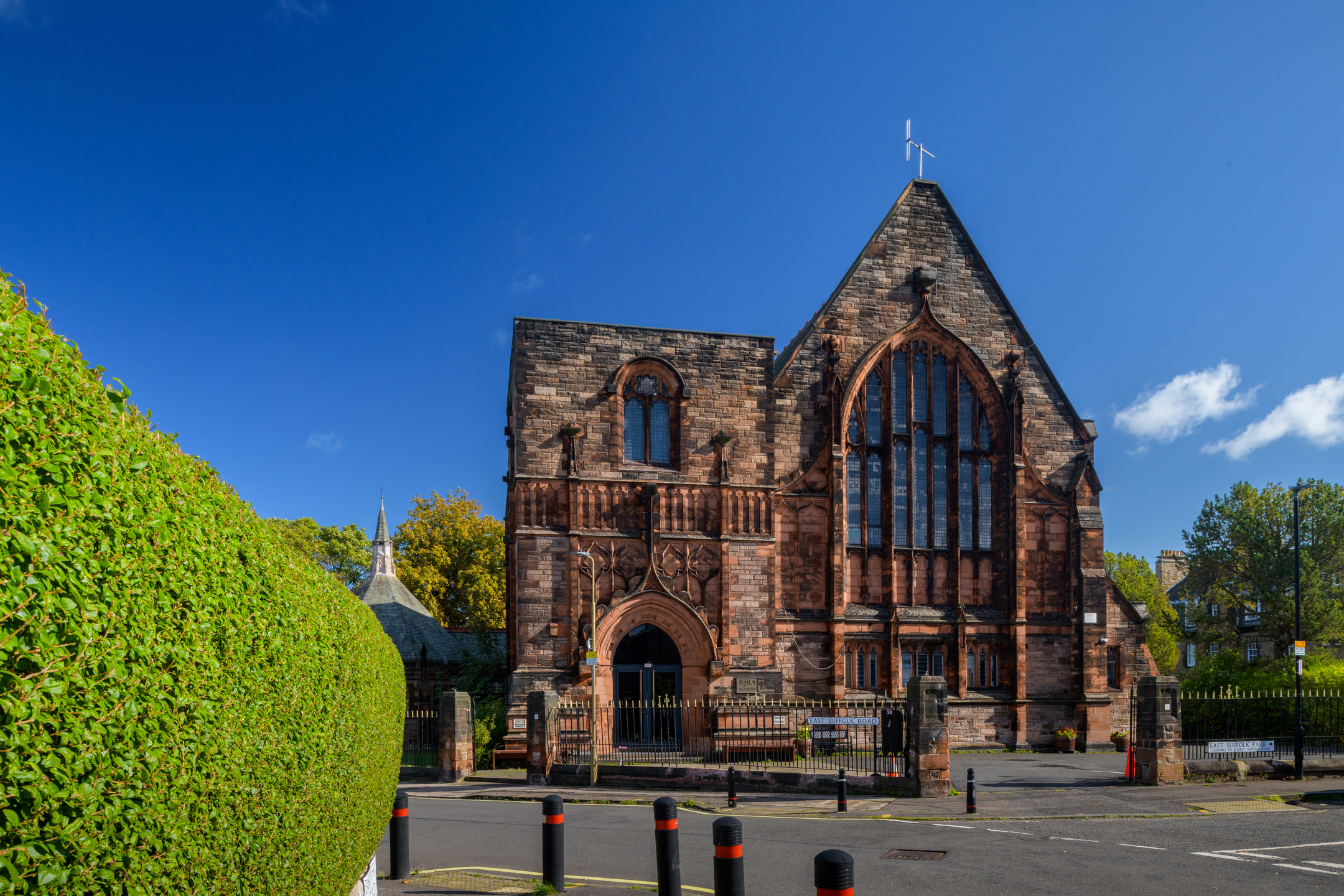 Front view of a large red sandstone church or chapel with Gothic-style arched windows and entrance, viewed from across a quiet road.