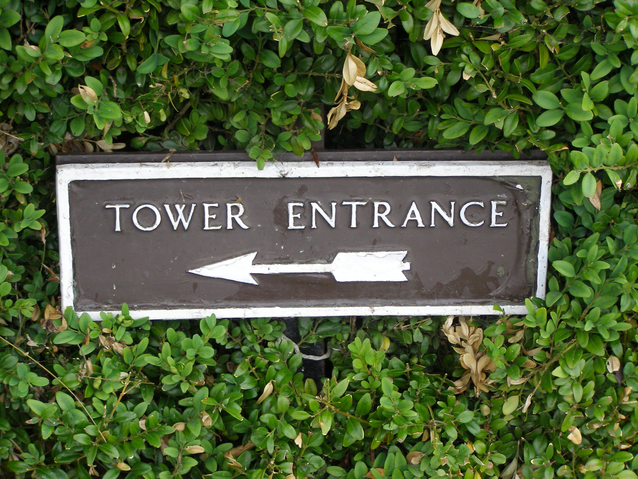 An old fashioned metal sign which uses a historic-looking arrow design to direct people to a tower entrance