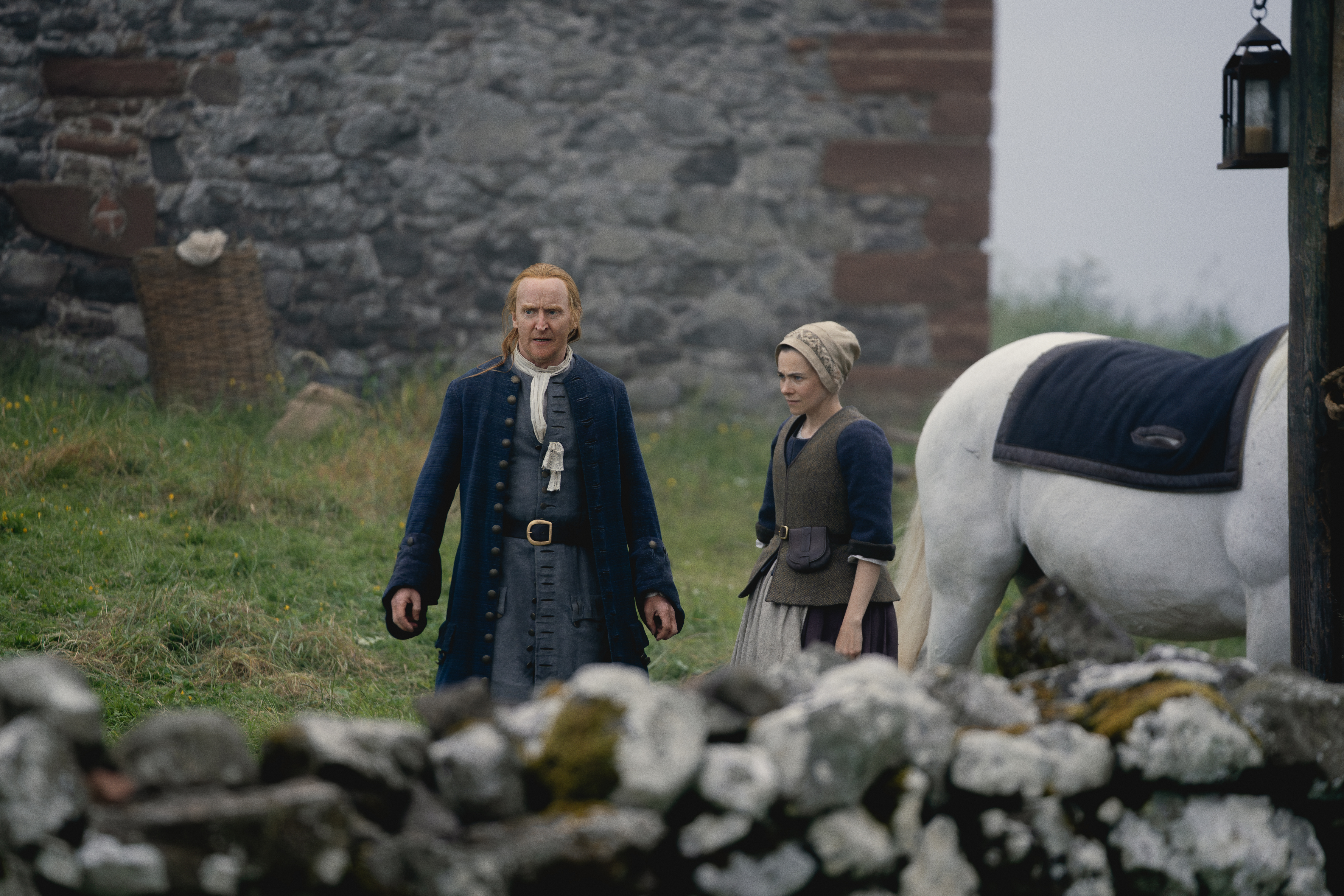 Two actors and a horse in front of a stone castle wall.