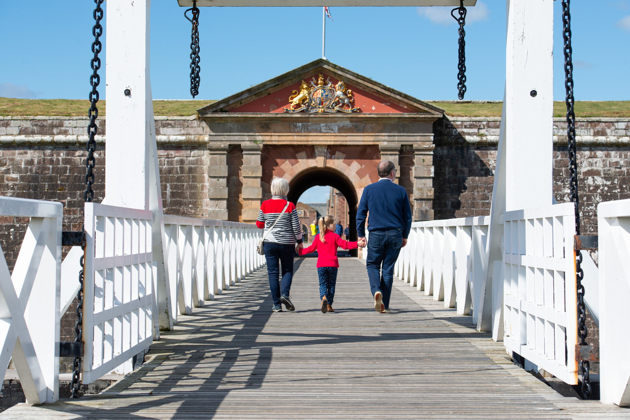 A family crosses a wooden bridge at the entrance to a large military fort.
