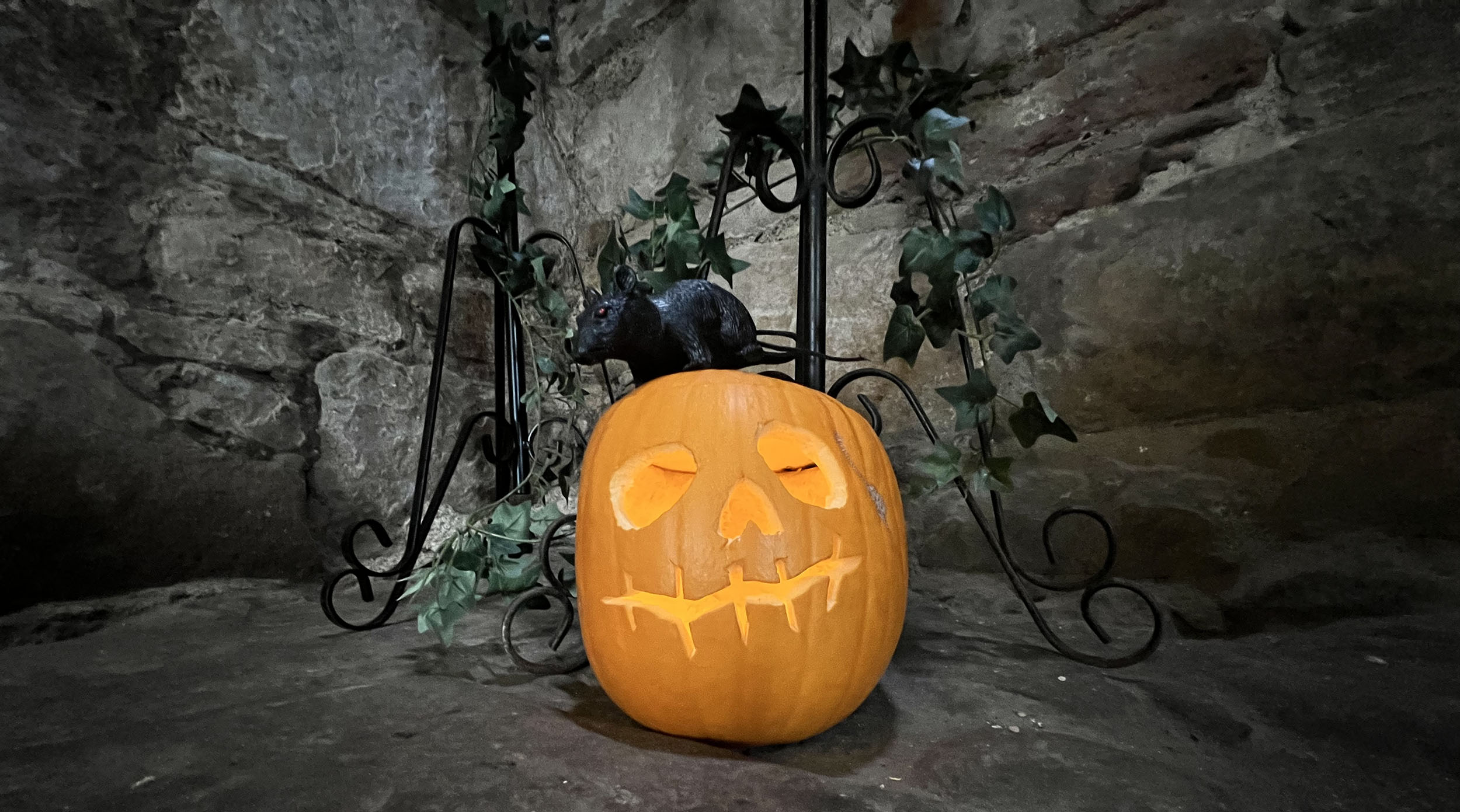 A carved pumpkin surrounded with ivy leaves and a pretend rat sitting on top of it